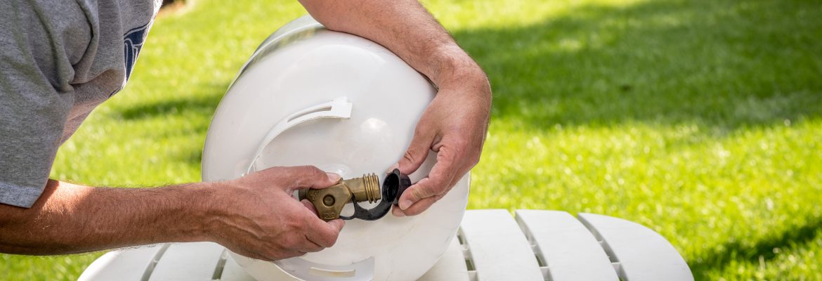 In The Backyard A Man Replaces The Cap On A Propane Bottle