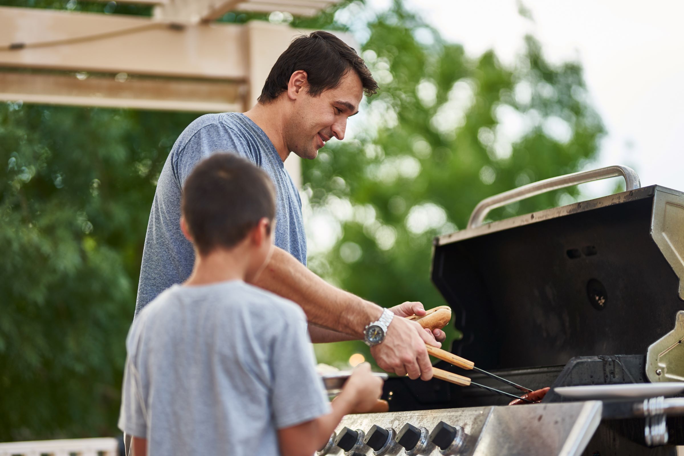 Father And Son Grilling Hot Dogs Together In Backyard