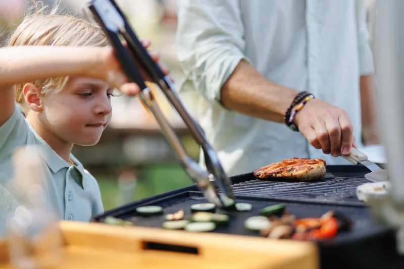 Young Boy Turning Grilled Vegetables With Tongs Young Boy Turning Grilled Vegetables With Tongs